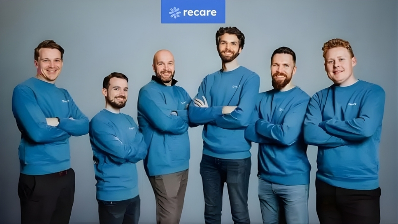 Group of six people in blue Recare shirts posing against grey background